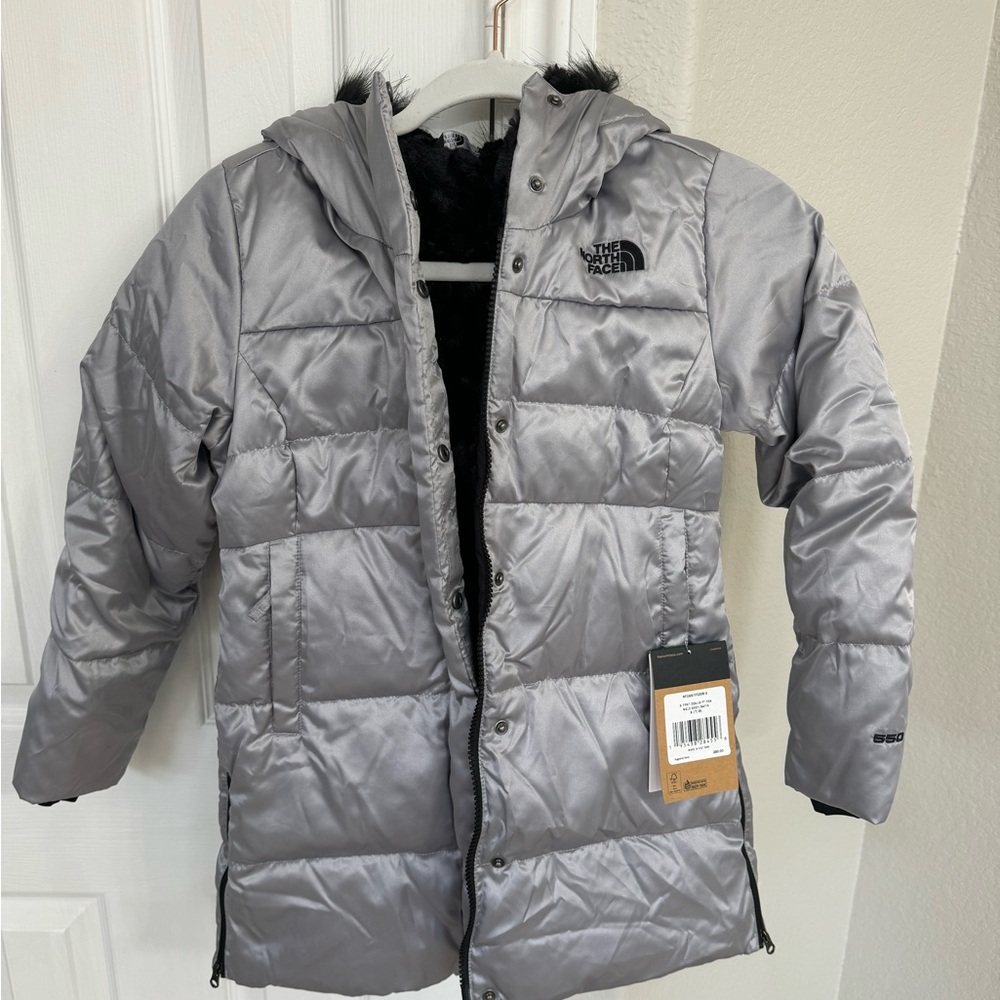Girls The North Face silver long puffer coat. Black faux fur lining inside.